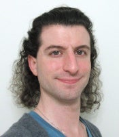 Photograph of Grey Pierce, a white nonbinary person with shoulder-length curly brown hair